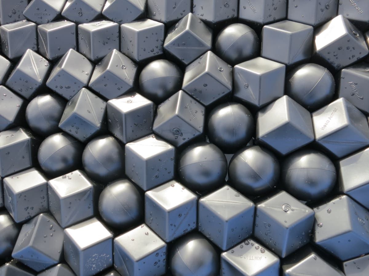 A tightly close-packed mix of AWTT's grey spherical Armor Ball floats and angular cube-shaped Hexa Armor floats, beaded with water droplets, viewed from directly above.
