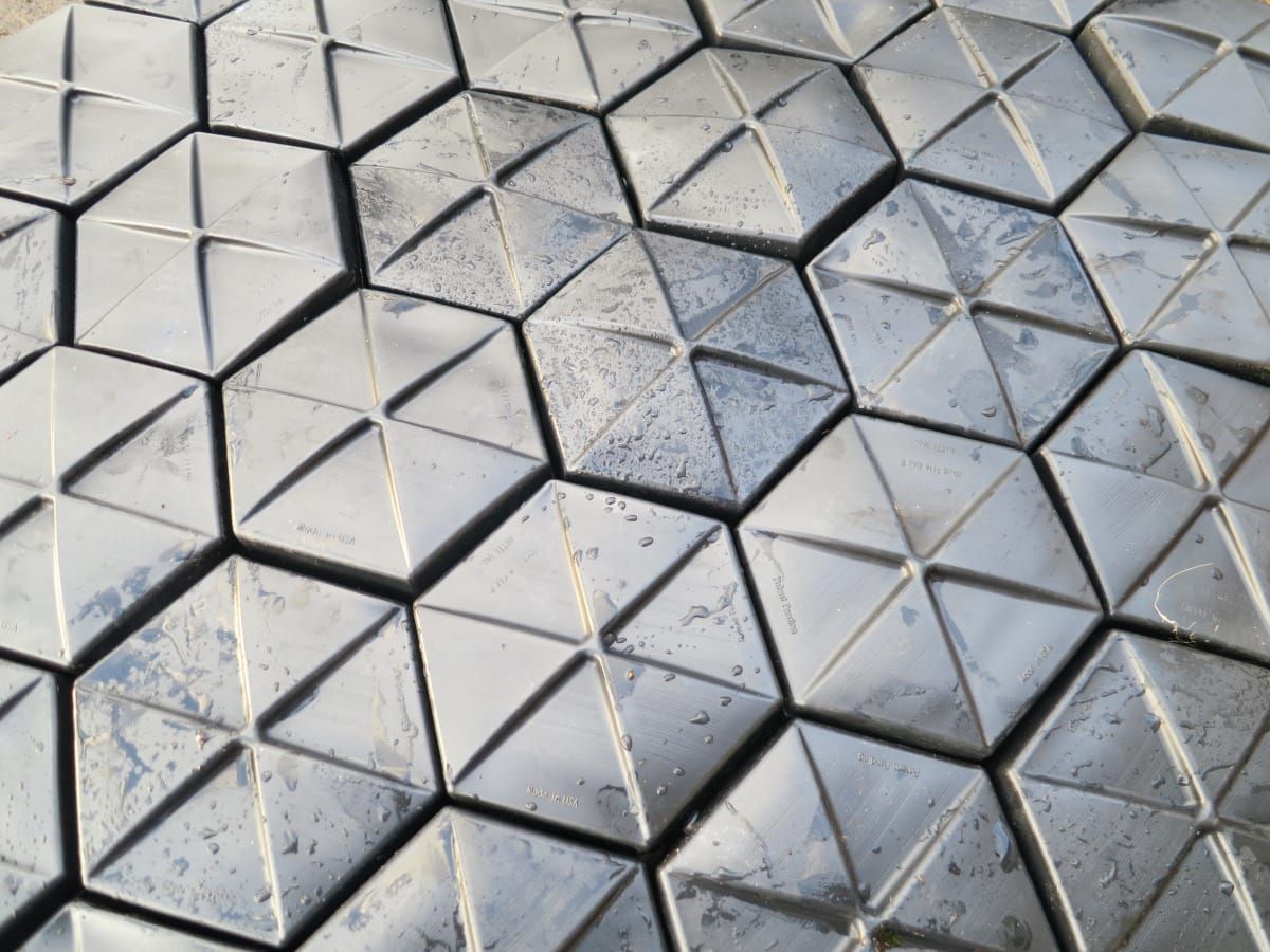 A close-up of black moulded hexagonal floating-cover tiles tessellated edge-to-edge in a uniform honeycomb pattern, each tile showing the raised central dome divided into six triangular facets.